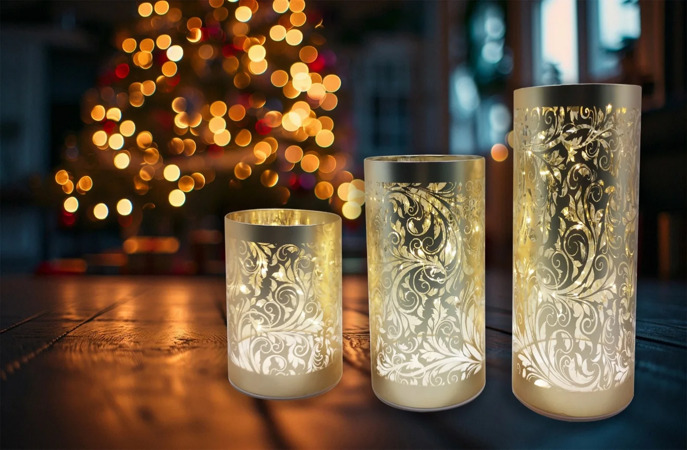 Three illuminated cylindrical glass candle holders with decorative cutout patterns